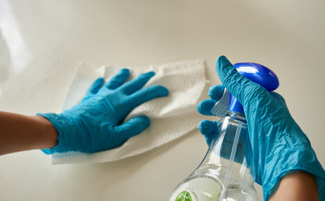 Close-up of gloved hands using disinfectant spray and cloth for cleaning surface.