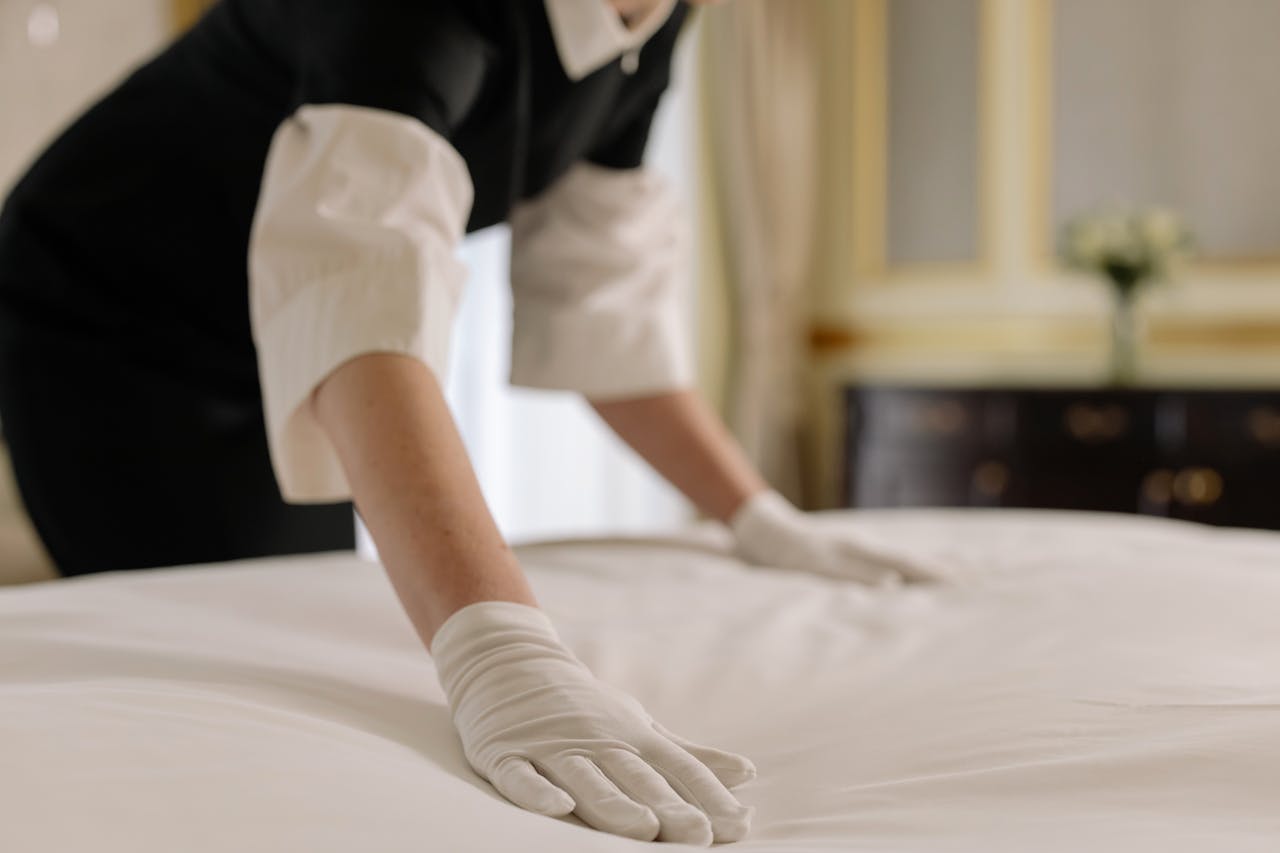 Home A housekeeper straightening the bed linens in a well-appointed hotel room.